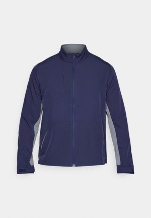 Marineblå softshell-jakke med grå sidepaneler, hævet krave, fuld lynlås og to forlommer. Glat tekstur med et funktionelt design.