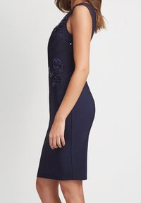 Marineblaues, figurbetontes Kleid mit Blumenstickereien an Schulter und Taille. Glatter Stoff mit ärmellosem Design und knielangem Schnitt.