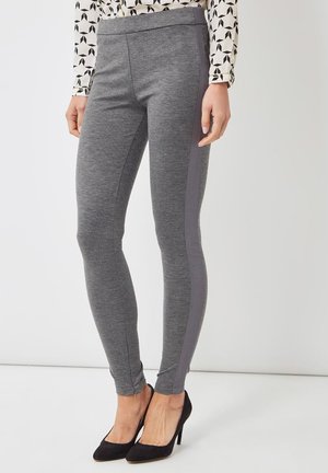Leggings grises con una textura suave, que presentan un panel lateral gris oscuro y una cinturilla elástica. Combinadas con tacones altos negros.