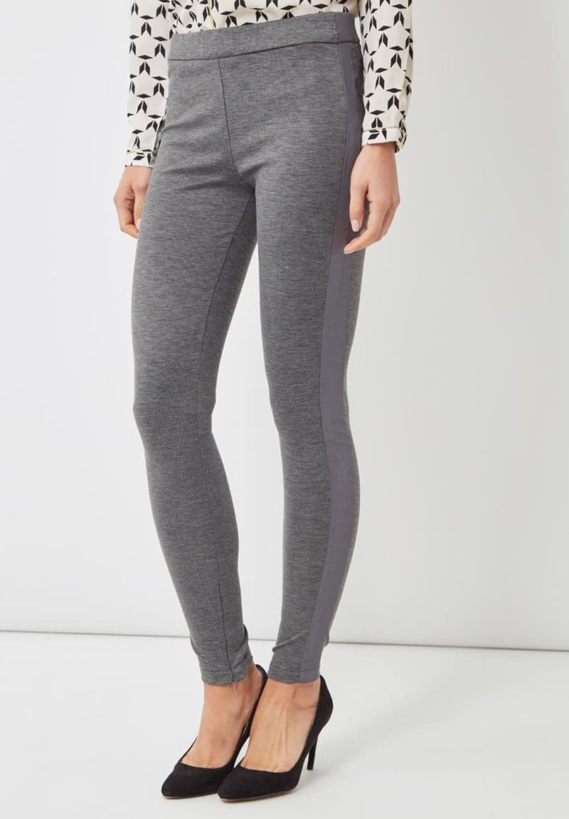 Leggings grises con una textura suave, que presentan un panel lateral gris oscuro y una cinturilla elástica. Combinadas con tacones altos negros.