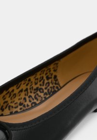 Čierna kožená balerína s hladkým vonkajškom a leopardím vzorom na podšívke. Má zaoblenú špičku a pružnú podrážku.