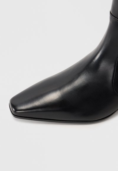 Black leather ankle boot with a pointed toe and smooth texture, featuring minimal stitching and a sleek silhouette.
