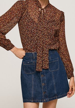 Ruskea kukkakuvioinen pitkähihainen pusero, jossa solmimisnauha kaulassa, yhdistetty nappilistallinen farkkuhame suuriin etutaskuihin.