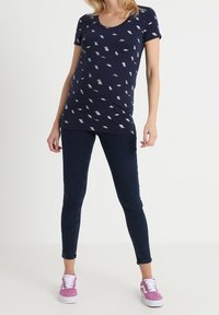 Camiseta de manga corta de color azul marino con escote redondeado y patrones de hojas blancas dispersas, combinada con jeans ajustados oscuros y zapatillas rosas.