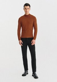 Brązowy, dopasowany sweter z golfem z fakturowanej dzianiny, zestawiony z czarnymi spodniami typu slim-fit i błyszczącymi czarnymi botkami za kostkę.