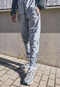 Light blue track pants with zippers, featuring a logo on the hip. Gray athletic shoes with mesh details and a textured sole.