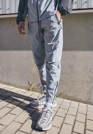 Lichtblauwe sportbroeken met ritsen, voorzien van een logo op de heup. Grijze sportschoenen met gaasdetails en een gestructureerde zool.
