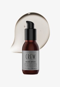 Flacon de sérum pour barbe American Crew avec distributeur pompe noir et goutte de liquide clair en arrière-plan, étiqueté 1,7 fl oz 50 ml.