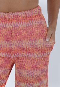 Pantaloni colorati a zigzag in tessuto rosa, arancione e giallo. Presentano un elastico in vita e tasche laterali, mostrando un design testurizzato.