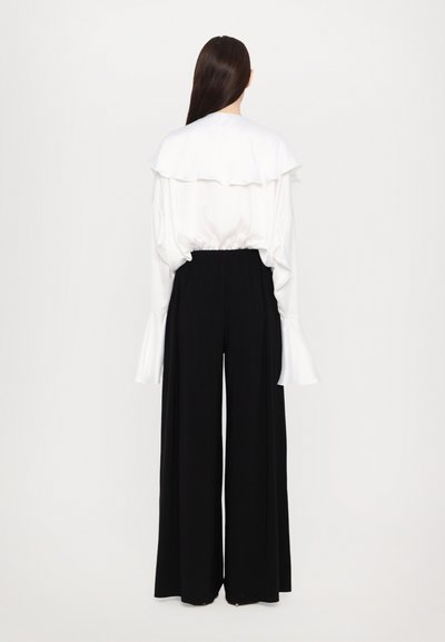 Witte blouse met gelaagde ruffel kraag en brede mouwen, gecombineerd met zwarte, hoog-waist, wijde broekspijpen. Gladde stofstructuur.