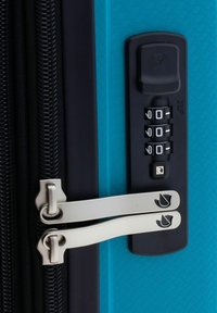 Maleta rígida con un exterior de color turquesa vibrante, patrón texturizado, dobles cremalleras y un candado de combinación incorporado.