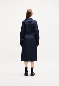 Jeansklänning med långa ärmar, midjebälte och rak nederkant. Mörkblå färg med subtila sömdetaljer på baksidan.
