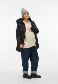 Crna puhasta jakna, kremasti top, plave traperice s podvrnutim rubom i crne čizme. Topla siva pletena kapa. Model prikazuje trudnički oblik.