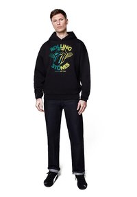 Czarny hoodie z kolorowym logo Rolling Stones, zawierający wzór języka, kieszeń kangurzą oraz luźny krój, połączony z ciemnymi dżinsami.
