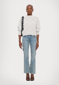 Maglione lavorato a maglia grigio chiaro a scacchi, jeans blu a gamba dritta, sandali con tacco neri e cinturini, e una borsa nera con accenti circolari.