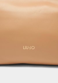 Tan lædertaske med glat tekstur, prydet med et subtilt logo "LIU•JO" i guld nederst til højre. Enkel, minimalistisk design.