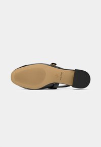 Black leather shoe with a rubber sole, featuring a rounded toe, adjustable strap, and subtle logo embossing on the insole.