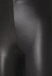 Zwarte leggings met een gladde, glanzende textuur; aansluitend ontwerp; minimale stiksels op de naden, wat een slanke, gestroomlijnde uitstraling benadrukt.