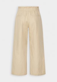 Pantalons larges beiges avec une taille élastiquée, fabriqués en tissu léger, dotés de deux poches arrière et d'une texture lisse.