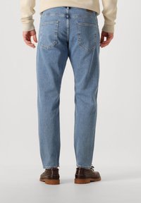 Jeans de mezclilla azul claro con corte recto, con dos bolsillos traseros y diseño minimalista, combinados con zapatos marrón oscuro con cordones.