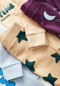 Beige, lila und hellblaue Baumwoll-Sweatpants mit gerippten Bündchen. Ein Paar hat grüne Sterne und blaue grafische Designs.