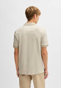Polo beige en tissu texturé, doté d'un col court et d'un subtil détail de couture au dos, associé à un pantalon beige.