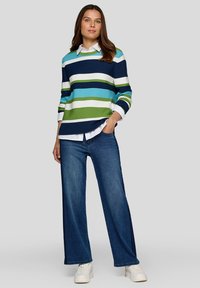 Gestreifter Strickpullover in Blau, Grün und Weiß, kombiniert mit einem weißen Hemd mit Kragen, dazu weiter geschnittene blaue Jeans und weiße Sneakers.