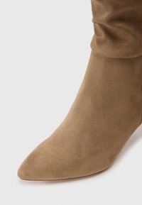 Stivale alla caviglia in suede marrone con punta a forma di mandorla e design superiore morbido. Texture soffice e finitura senza cuciture. Adatto a vari outfit.