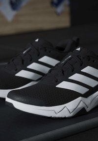 Μαύρα και λευκά παπούτσια για τρέξιμο Adidas με τρεις λευκές ρίγες και ζιγκ-ζαγκ σχέδιο στη σόλα, ακουμπισμένα σε σκοτεινή επιφάνεια.