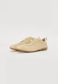 Beige sømdæmpede sko med lav profil, snørebånd design, perforerte detaljer og gummisåle. Har en liten hælflik for enkel påkledning.