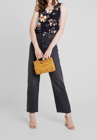 Blommig marinblå blus, högmidjade svarta jeans och en gul korghandväska. Öppen tå-klackar och lager av halsband fulländar outfiten.