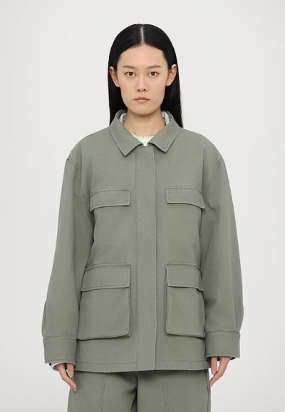 Grüne Baumwolljacke mit Kragen, Frontreißverschluss und zwei großen Brusttaschen, locker sitzend und mit sichtbaren Steppdetails.