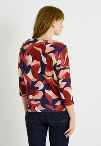 Top de tres cuartos en color marino con un patrón floral geométrico en tonos rojos y rosas. Fabricado con una tela suave y texturizada.