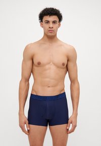 Tamnoplave muške bokserice s kontrastnom plavom elastičnom trakicom na kojoj je u debelim slovima ispisano ime branda "UNDER ARMOUR".