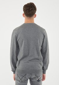 Maglione grigio lavorato a maglia con maniche lunghe e scollatura rotonda, con polsini e orlo a coste, visto da dietro.