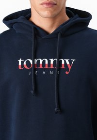 Marineblauwe hoodie met een trekkoord, voorzien van een prominent weergegeven wit en rood 'tommy jeans' logo. Glad katoen. 