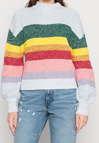 Pull en tricot avec un col montant arborant de larges rayures horizontales vertes, jaunes, rouges, roses et bleues. Texture douce avec des manches bouffantes.