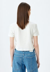 Witte cropped t-shirt met korte mouwen, gemaakt van zachte katoen. Te combineren met hoog-waisted blauwe denim jeans met grote achterzakken.