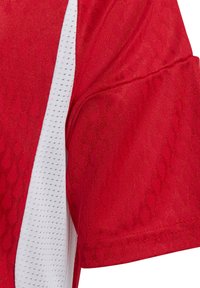 Camiseta deportiva roja con tejido texturizado y un patrón, y un panel de malla blanca a lo largo del costado. Incluye mangas cortas y un cuello redondo.