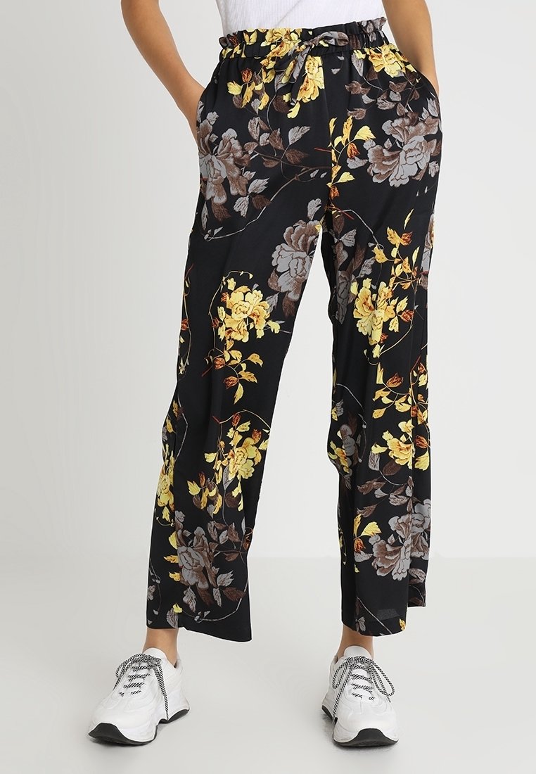 Pantalon noir à jambes larges avec imprimé floral jaune et marron porté avec des baskets blanches et un haut blanc.