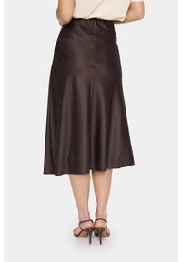 Brun satin midi kjol med en utsvängd form, utrustad med ett gummiband i midjan och en mjuk textur, i kombination med sandaler med remmar.