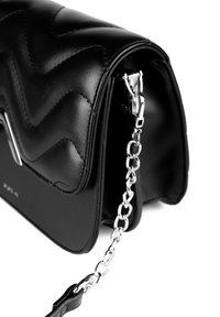 Schwarze Handtasche aus Kunstleder mit einem gesteppten Zickzackmuster, silberner Kettenriemen und einem Reißverschluss. Auffällig durch ihre strukturierte Form und glatte Textur.