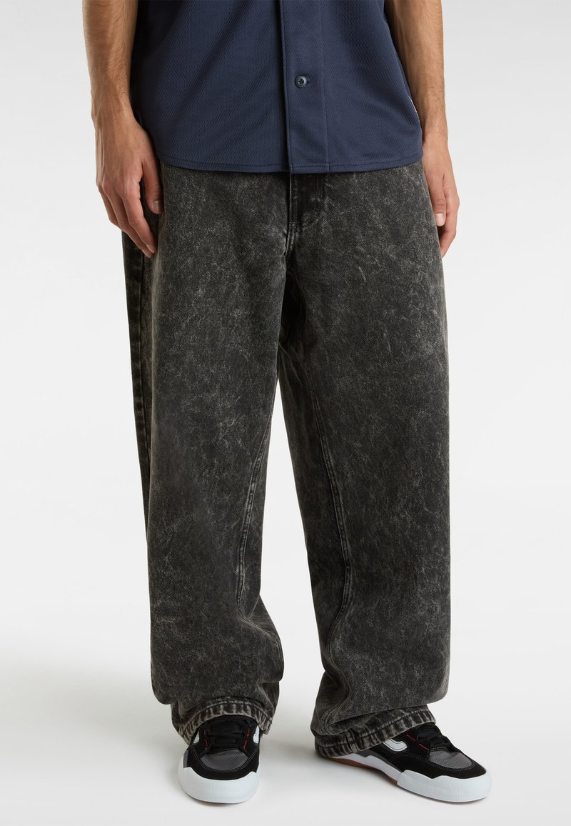 Baggy sorte denim jeans med en falmet tekstur, der har en løs pasform og synlige stikninger. Sammen med sorte og hvide sneakers.