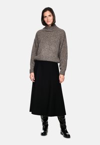 Pull en maille gris avec un col haut ; associé à une jupe noire évasée et des bottines noires brillantes. Design minimaliste, texture douce.