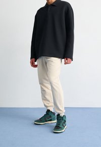 Överdimensionerad svart polo, beige joggers och gröna/svarta högskor. Materialet verkar mjukt med en avslappnad passform och minimal design.