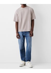 T-shirt beige a maniche corte con scollo rotondo abbinata a jeans azzurri a gamba dritta e sneakers bianche. Stile semplice, vestibilità rilassata, senza fantasie.