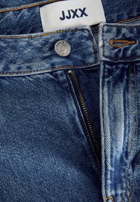 Τζιν παντελόνι με φερμουάρ, μεταλλικό κουμπί με λογότυπο και αντίθετες πορτοκαλί ραφές. Το ύφασμα έχει μέτριο πλύσιμο και απαλή υφή.