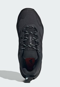 Scarpa atletica nera con tomaia in mesh testurizzato, lacci a contrasto e collo imbottito. Presenta il logo e una suola in gomma. Vista dall'alto, accenti minimi.