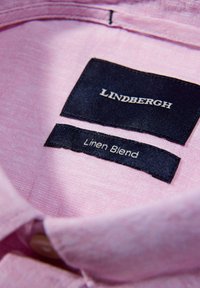 Lichtroze linnen blend overhemdkraag met marineblauwe stoffen labels met de tekst "LINDBERGH" en "Linen Blend" in witte letters. Subtiele textuur zichtbaar.