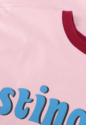 Close-up of pink fabric with part of blue text "stin" and a red ribbed collar on clothing.